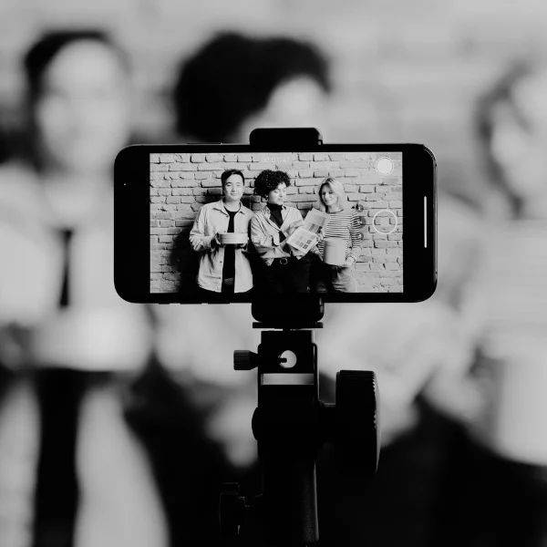 Phone on tripod showing three people posing against a brick wall, holding mugs.